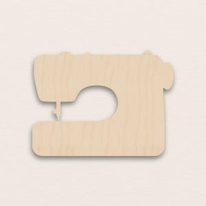 May include: A light brown wooden sewing machine cutout. The design features a curved arm, a large circular opening, and a needle. This craft supply is ideal for sewing and crafting projects.
