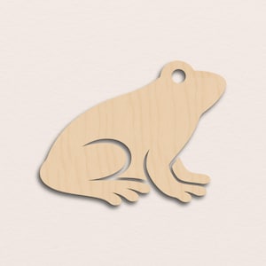 Könnte beinhalten: Ein Holzfrosch-Ausschnitt mit natürlicher Holzmaserung. Der Frosch ist im Profil dargestellt, mit detaillierten Beinen und Körper. Oben befindet sich ein kleines Loch, wahrscheinlich zum Aufhängen. Der Frosch hat eine hellbraune Farbe.