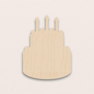 Op de afbeelding: Houten uitgesneden afbeelding van een verjaardagstaart met twee lagen en drie kaarsen. De taart is gemaakt van lichtgekleurd hout en heeft een eenvoudig ontwerp. De kaarsen zijn ook van hout en staan bovenop de taart.