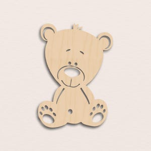 May include: A light brown wooden teddy bear cutout. The bear has a smiling face, sitting posture, and paw details. Ideal for crafts or decorative purposes, the bear is made of wood.