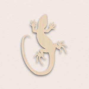 Puede incluir: Recorte de madera con forma de lagarto de color marrón claro. El lagarto tiene una cola larga, cuatro patas y un cuerpo detallado. El recorte es un elemento decorativo, adecuado para manualidades o decoración del hogar.