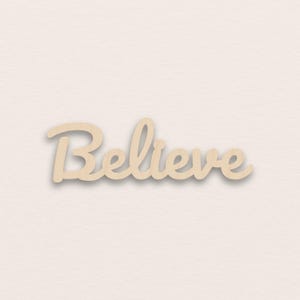 Op de afbeelding: Houten bord met het woord "Believe" in een cursief lettertype. Het bord is gemaakt van lichtgekleurd hout en heeft een licht schaduweffect, waardoor het een driedimensionale uitstraling heeft. De achtergrond is effen en neutraal.