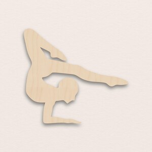 Può includere: Sagoma in legno di una ginnasta in posizione di handstand. La figura è in equilibrio, con un braccio e una gamba tesi. Il ritaglio è in legno chiaro e ha una finitura liscia.