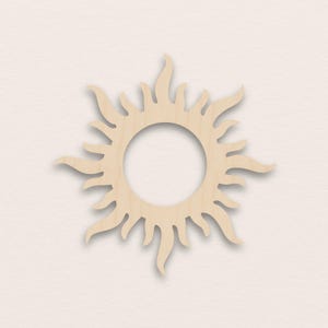 May include: A wooden sunburst cutout with a central circular opening. The sun's rays are stylized with pointed and curved edges, creating a decorative design. The wood has a natural, light tan color.