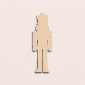 May include: A light brown wooden nutcracker soldier cutout. The figure has a tall hat, arms, and legs, with a simple design. The cutout is standing upright, with a shadow beneath it.