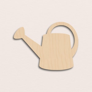 May include: A wooden watering can cutout, featuring a spout, a rounded body, and a curved handle. The cutout is made of light-colored wood and is designed for crafting or decorative purposes. The watering can is a gardening-themed item.