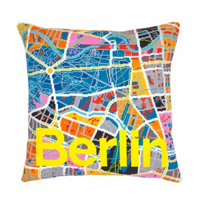 Può includere: Un cuscino colorato con una mappa di Berlino stampata su di esso. La parola "Berlino" è ricamata in giallo sul cuscino.