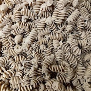 May include: A close-up of a large quantity of brown, dried pasta. The pasta is in the shape of a spiral, or a corkscrew.