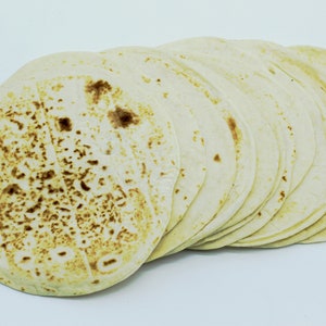 May include: A stack of round, white tortillas, some of which have a lightly browned surface.