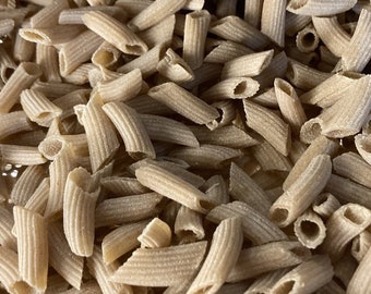May include: A close-up view of a pile of brown penne pasta. The pasta is dry and uncooked.