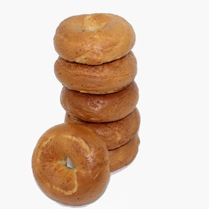 May include: A stack of six plain bagels, with one bagel laying on its side in front of the stack.