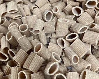 May include: A close-up view of a large pile of dried pasta. The pasta is a light brown colour and has a ridged texture. The pasta is shaped like short tubes.