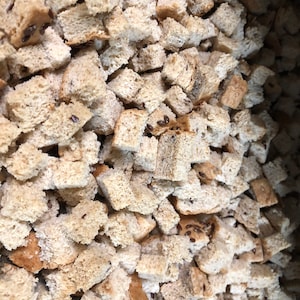 May include: A close-up image of a large bowl filled with toasted bread cubes. The cubes are a light brown color and appear to be made from white bread.