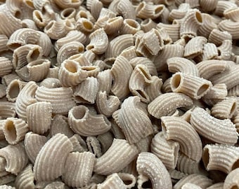 May include: A close-up of a large quantity of uncooked elbow macaroni pasta. The pasta is a light brown colour and has a rough texture.