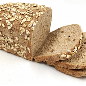 May include: A loaf of brown bread with oats on top, sliced into four pieces. The bread is on a white surface.