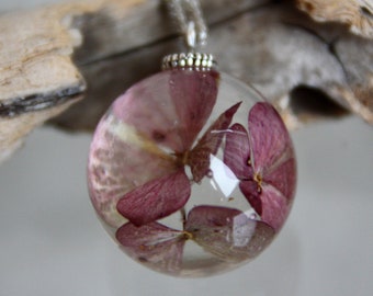 May include: A silver chain necklace with a clear glass pendant containing pink pressed flowers.