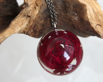 May include: A silver chain necklace with a round, clear pendant filled with red and white swirls. The pendant is approximately 2.5 cm in diameter.