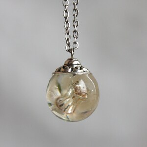 May include: A silver chain necklace with a clear glass orb pendant containing a dried flower. The orb has a silver filigree design around the top.