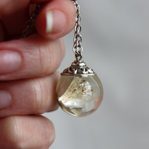 May include: A silver chain necklace with a clear glass orb pendant containing dried flowers. The orb has a silver filigree design around the top.