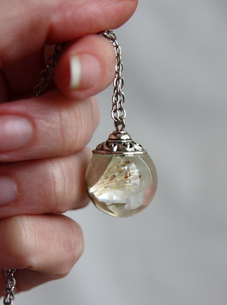 May include: A silver chain necklace with a clear glass orb pendant containing dried flowers. The orb has a silver filigree design around the top.