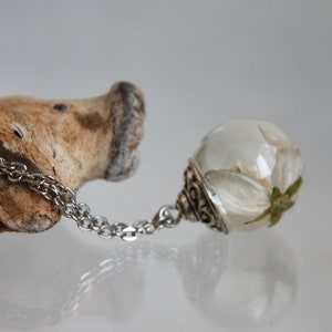 May include: A silver chain necklace with a clear glass pendant containing a white flower. The pendant has a silver ornate design around the edge.