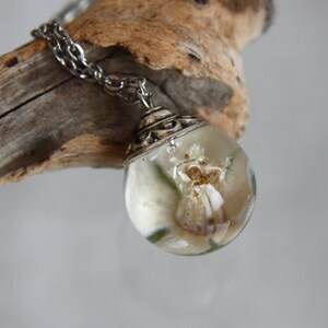 May include: A silver chain necklace with a clear glass pendant containing a preserved white flower.