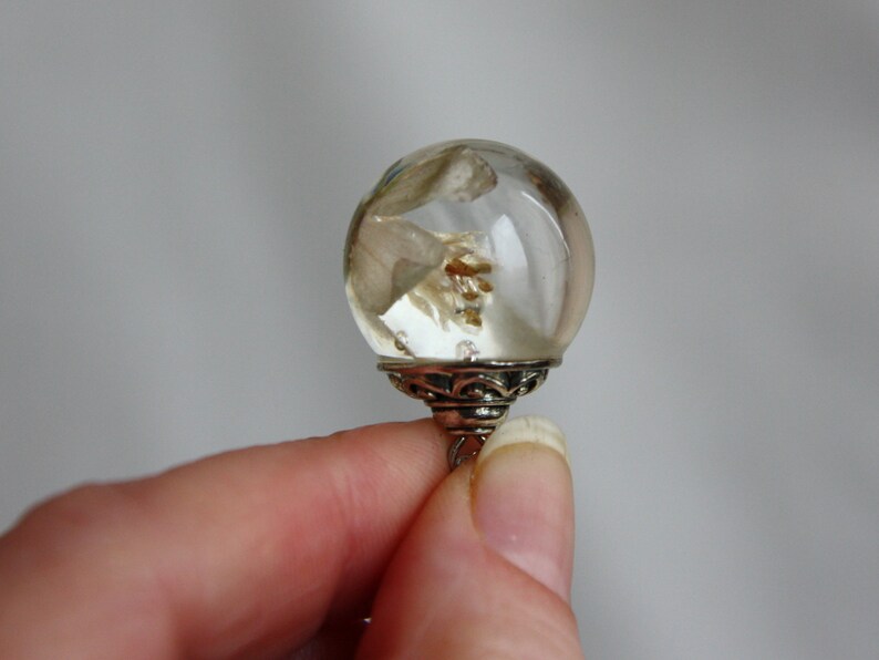 May include: A clear glass sphere with a silver base, containing dried flowers and botanicals.