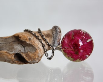 May include: A silver chain necklace with a round pendant featuring a preserved pink flower encased in clear resin.