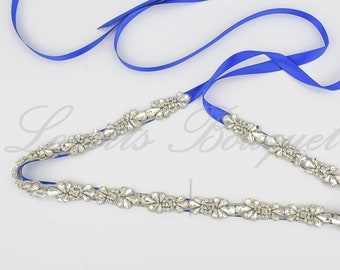 May include: A decorative belt featuring a long, vibrant royal blue satin ribbon adorned with a continuous row of clear, faceted crystals arranged in floral-inspired patterns. The crystal embellishment is centred on the ribbon, creating a sparkling effect.