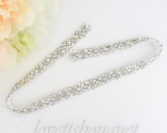 May include: A silver bridal sash featuring a delicate design of clear rhinestones arranged in a floral pattern.