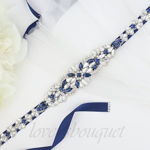 May include: Navy blue satin ribbon with a silver and blue rhinestone embellishment. The embellishment features a cluster of clear and blue rhinestones in a floral design.