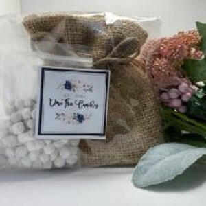 May include: A small burlap bag filled with white wax melts. The bag has a white label with the text "Uni The Cozy" and a floral design.