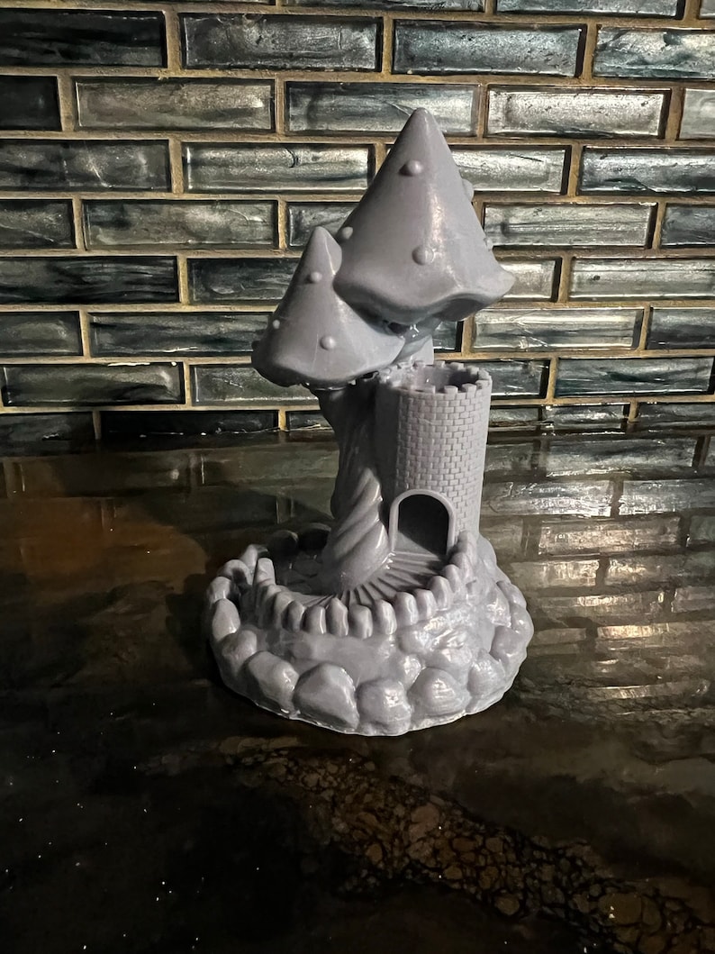May include: A gray 3D printed mushroom castle with a winding staircase leading to the top. The castle is surrounded by a base of rocks.