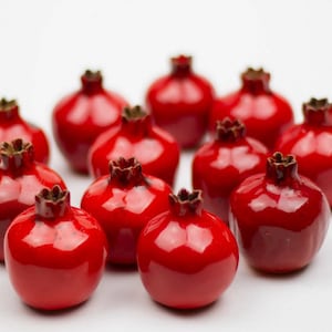 Może przedstawiać: Grupa 11 małych, czerwonych, ceramicznych ozdób w kształcie granatów. Granaty są ułożone w kółko na białym tle.
