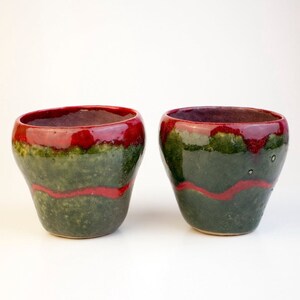 May include: Two ceramic cups with a green and red glaze. The cups are round and have a wide opening.