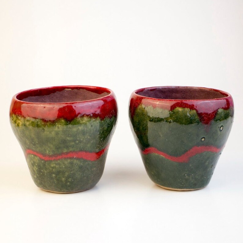 May include: Two ceramic cups with a green and red glaze. The cups are round and have a wide opening.