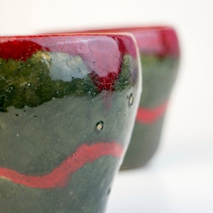 May include: Two ceramic mugs with a green and red glaze. The mugs have a crackled finish and a unique, abstract design.