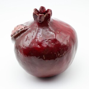 Puede incluir: Una figurita de cer&aacute;mica roja de granada con un acabado brillante. La figurita est&aacute; detallada con una parte superior texturizada y una superficie ligeramente irregular.