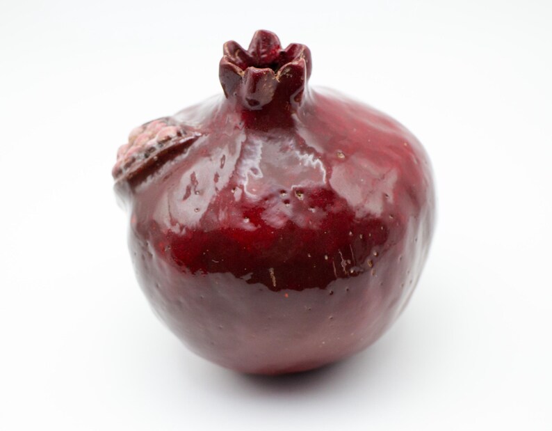 Puede incluir: Una figurita de cer&aacute;mica roja de granada con un acabado brillante. La figurita est&aacute; detallada con una parte superior texturizada y una superficie ligeramente irregular.