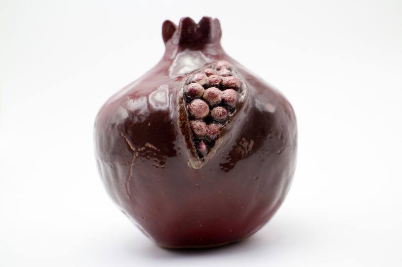 Puede incluir: Un jarr&oacute;n de cer&aacute;mica de color rojo oscuro en forma de granada con un dise&ntilde;o detallado de una fruta de granada en su interior.