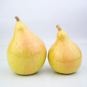 May include: Two ceramic pears, one larger than the other, are displayed on a white surface. Both pears are yellow with a speckled pink glaze.