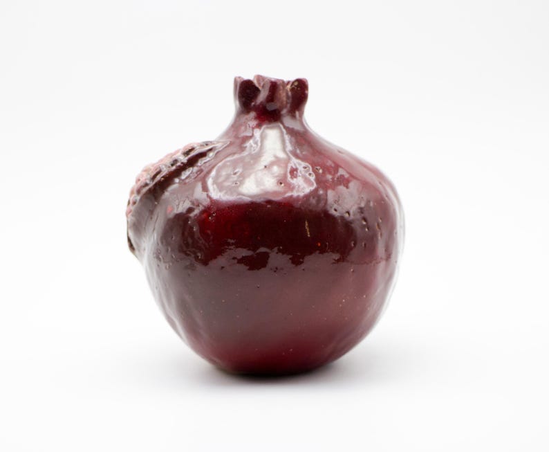Puede incluir: Un jarr&oacute;n de cer&aacute;mica de color rojo oscuro con un acabado brillante. El jarr&oacute;n tiene forma de granada con un tallo detallado y una superficie ligeramente irregular.