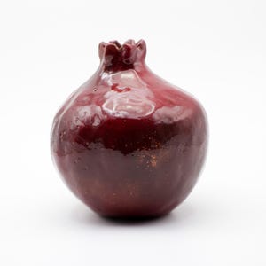 Puede incluir: Un jarr&oacute;n de cer&aacute;mica de color rojo oscuro en forma de granada con un acabado brillante. El jarr&oacute;n tiene una forma redondeada y una superficie ligeramente texturizada.