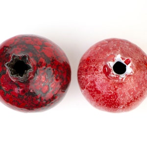 May include: Two red ceramic pomegranate ornaments with black and white speckled glaze. The ornaments are round and have a small opening at the top.