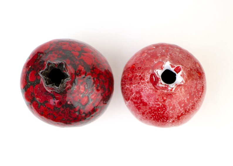 May include: Two red ceramic pomegranate ornaments with black and white speckled glaze. The ornaments are round and have a small opening at the top.