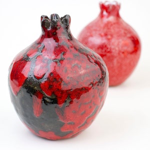 May include: Two red ceramic pomegranates, one with a black glaze, the other with a smooth finish.