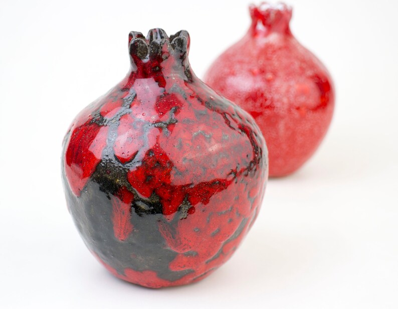 May include: Two red ceramic pomegranates, one with a black glaze, the other with a smooth finish.