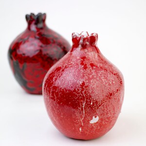 May include: Two ceramic vases shaped like pomegranates. One is red with white speckles and the other is red and black.
