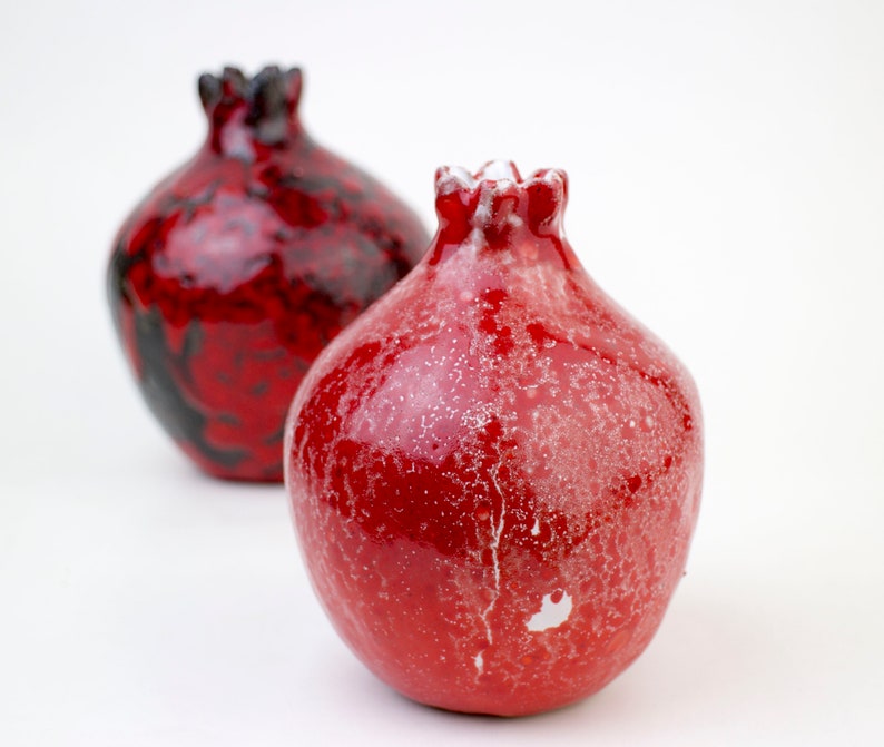 May include: Two ceramic vases shaped like pomegranates. One is red with white speckles and the other is red and black.