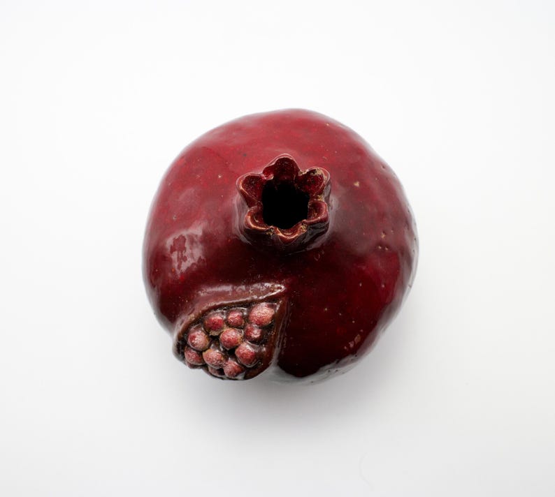 Puede incluir: Un jarr&oacute;n de cer&aacute;mica rojo en forma de granada con un dise&ntilde;o esculpido detallado. El jarr&oacute;n tiene una peque&ntilde;a abertura en la parte superior para flores u otros art&iacute;culos decorativos.